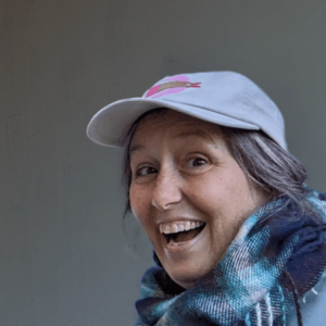a photo of a smiling middle aged woman wearing a ball cap and a scarf